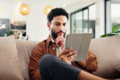 Un homme assis sur son canapé consulte des informations sur une tablette