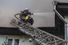 Un pompier professionnel projette un produit avec sa lance pour éteindre un incendie dans un logement depuis une échelle d'intervention