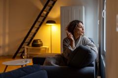 Une femme, assise sur son canapé, regarde par la fenêtre en fumant une cigarette