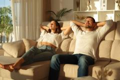 Jeune couple profite du soleil à l'aise dans le canapé du salon