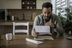 Un homme lit, préoccupé, le contenu d'un courrier qu'il vient de recevoir