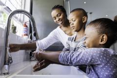 Une maman aide ses deux enfants qui se lavent les mains ensemble au lavabo de la salle de bain