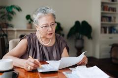 Une femme d'âge mûr vérifie ses factures sur sa table de salon, à l'aide de sa calculatrice