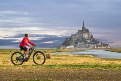 Touriste à vélo devant le Mont Saint-Michel, emblème de la Manche