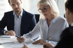 Une femme d'affaires signe un contrat en présence de deux hommes en costume