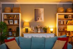 Petit salon cosy éclairé, avec un canapé bleu et des coussins rouges. 