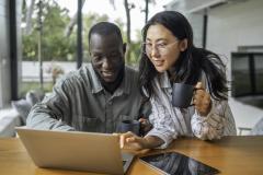 Un jeune couple complète un questionnaire en ligne sur un pc portable dans son salon