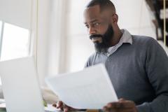 Un homme étudie des documents sur son pc portable, un document à la main