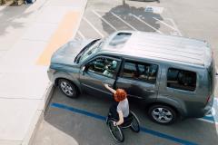 Une femme se déplaçant en fauteuil roulant ouvre la portière avant de son véhicule garé sur une place handicapé