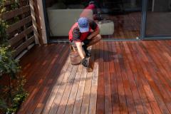 Un homme passe une couche de produit au pinceau sur une terrasse en bois pour la protéger et lui redonner de l'éclat