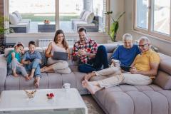 Une famille réunie sur le grand canapé d'angle gris qui consulte : ordinateurs et telephones...