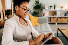 Une femme assise sur son canapé consulte un dossier sur sa tablette