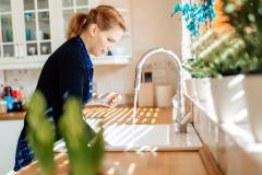 Une femme debout dans sa cuisine fait couler de l'eau dans son évier 
