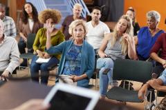 Une femme assise dans l'assemblée lève la main pour parler lors d'une assemblée générale de copropriété