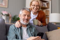 Un couple de retraités regarde des informations sur un téléphone portable dans son salon