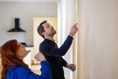 Un couple mesure la hauteur d'un mur de son logement à l'aide d'un mètre