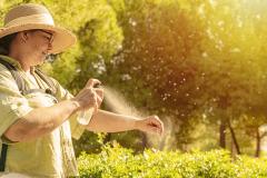 Une dame portant un chapeau vaporise un spray anti-moustiques sur son avant-bras, en extérieur