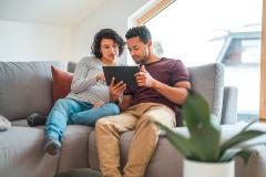 Un couple, dont la femme est enceinte, effectue des recherches sur tablette, installé sur son canapé