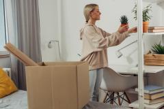 Une étudiante défait ses cartons et pose une plante sur une étagère pour la décorer