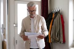 Un homme aux cheveux blancs lit un courrier qu'il vient de recevoir à son domicile