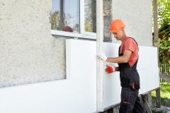 Un ouvrier du bâtiment réalise l'isolation extérieure d'une maison, en posant des panneaux isolants sur le mur extérieur