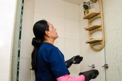 Une femme de ménage nettoie les murs carrelés d'une douche 