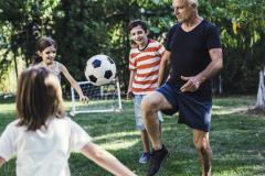 Des enfants jouent au foot dans leur jardin avec un homme d'âge mûr