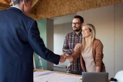 Un couple convient d'un accord avec un professionnel de la construction en lui serrant la main dans leur maison