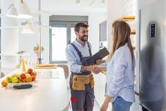 Une femme reçoit un ouvrier dans sa belle cuisine claire et lui serre la main. 