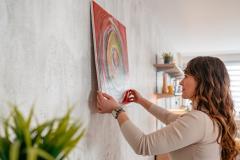 Une jeune femme aux cheveux longs ondulés accroche un cadre dans son salon, sans percer les murs