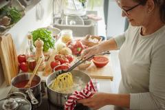 Une femme fait cuire des pâtes dans une grande casserole d'eau dans sa cuisine
