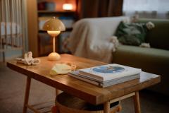 Petit appartement avec focus sur la table basse en bois brut, quelques livres et une lampe moderne jaune. 