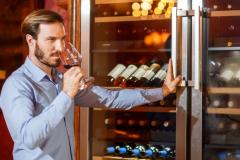 Un homme déguste un vin qu'il vient de choisir dans sa cave à vin réfrigérée
