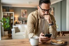 Un homme assis à la table de la cuisine apparait contrarié en lisant un message sur son téléphone