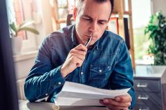 Un homme assis à son bureau vérifie avec attention le contenu du courrier qu'il tient dans la main