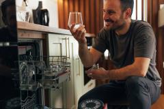 Un homme accroupi à côté de son lave-vaisselle admire la brillance de ses verres
