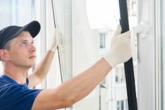 Un jeune professionnel en tenue de travail installe du double-vitrage sur la fenêtre d'un appartement