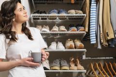 Une jeune femme admire son placard à vêtements et chaussures bien rangé, une tasse dans les mains