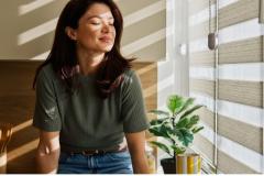Femme profitant du soleil du matin à la maison près des stores de fenêtre 