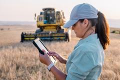 Une agricultrice tient une tablette numérique dans un champ agricole pour piloter son activité