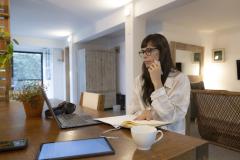 Femme brune travaillant sur son bureau, avec son ordinateur et une tasse de thé blanche.