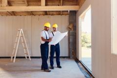 2 artisans en tenue de travail étudient un plan dans une maison en construction