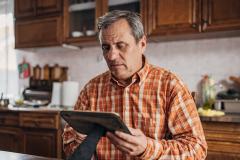 Un homme âgé se tient debout dans sa cuisine un peu ancienne, un cadre dans les mains
