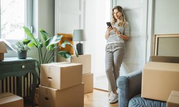 femme sur son téléphone dans un appartement entourée de cartons