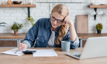 Femme blonde concentrée effectuant des calculs devant son pc, la tête en appui sur son bras