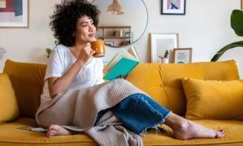 Célibataire assise sur son canapé avec à la main un livre et dans l'autre une tasse de thé