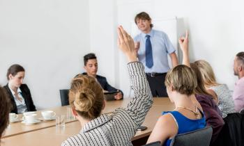 Des personnes sont réunies autour d'une table et lèvent la main pour voter, dans le cadre d'une réunion d'assemblée générale