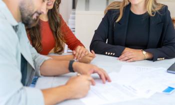 Un homme appose sa signature en bas d'un contrat en présence de deux femmes souriantes