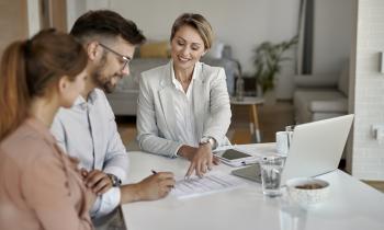 Un couple souriant signe le document que leur présente une femme.