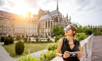 Une femme, un appareil photo à la main, devant la Cathédrale de Reims